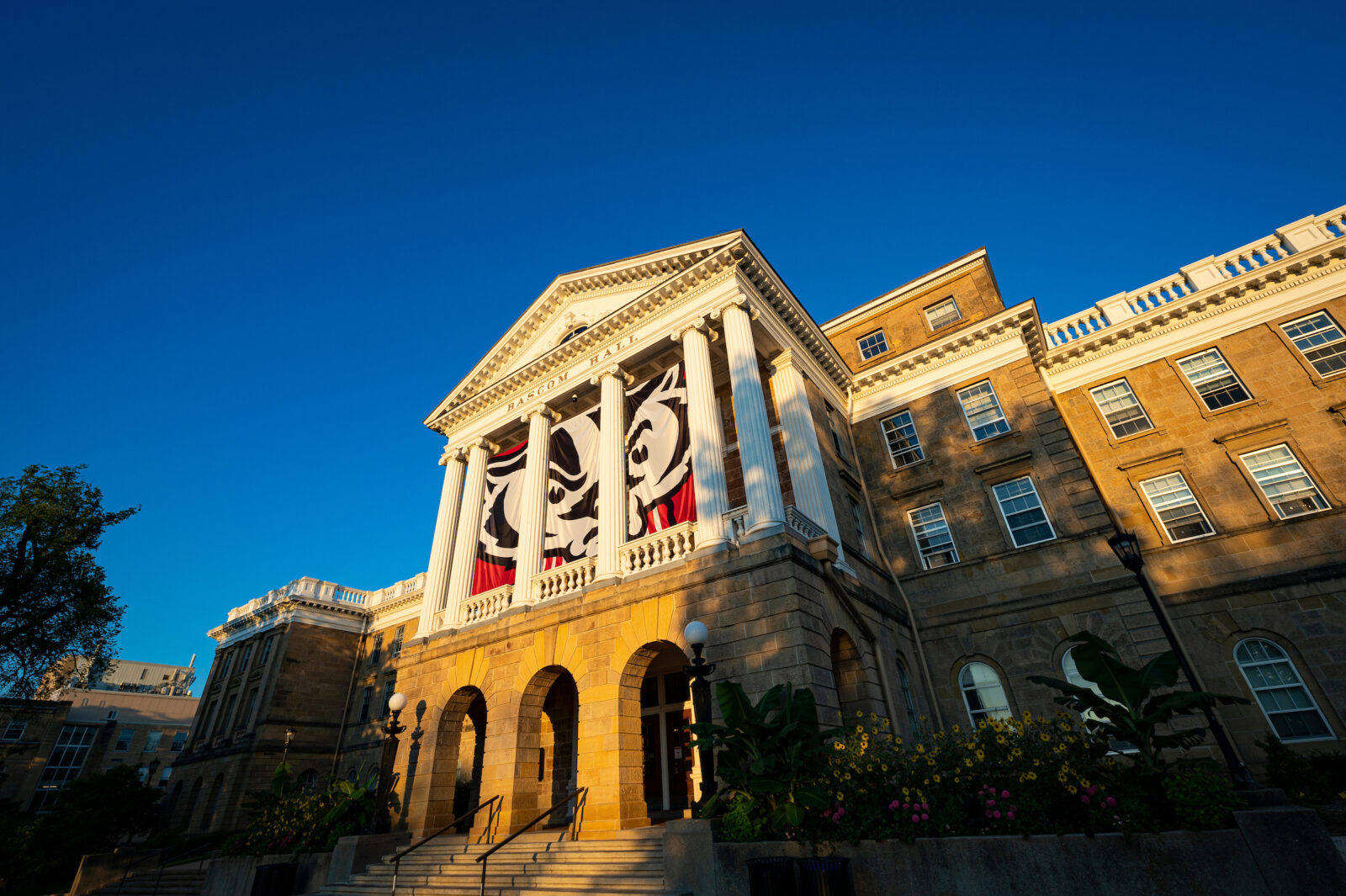Bascom Hall, featuring Bucky Badger banners, is pictured during sunrise with a deep blue sky in the background.